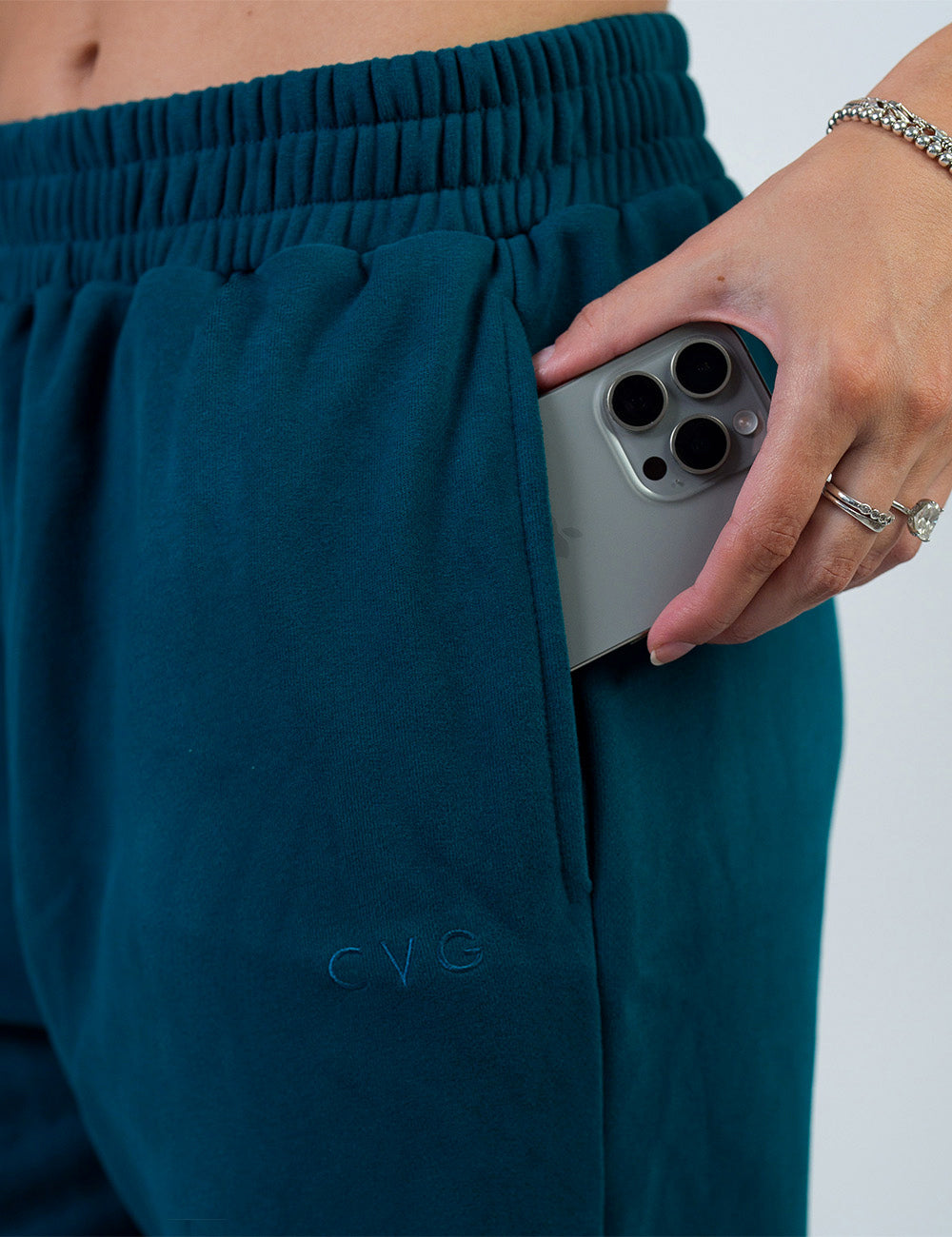 close up of the dark blue sweatpants with a subtle CVG logo holding a phone in its pocket