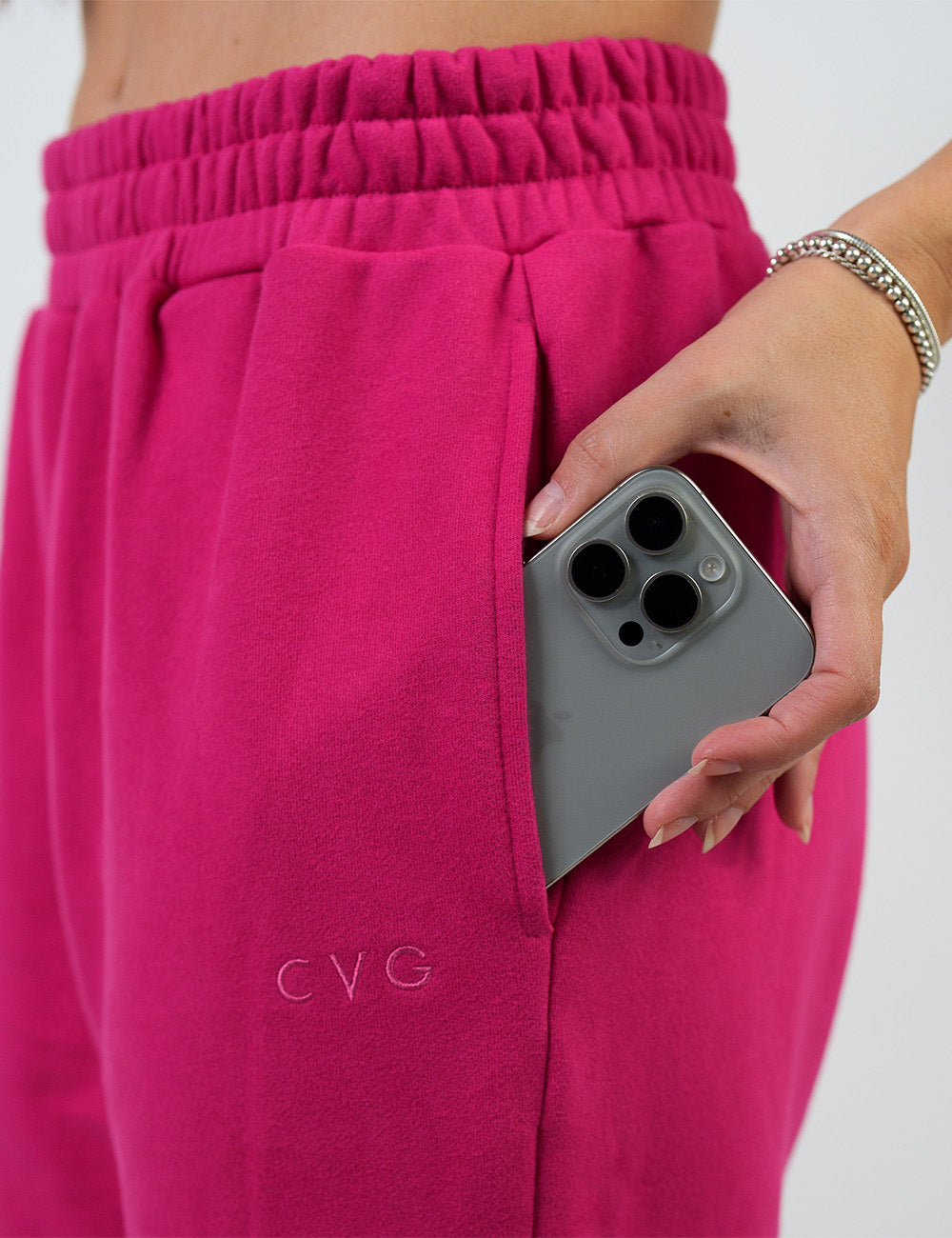 close up of the pink sweatpants with the subtle CVG logo holding a phone in its pocket