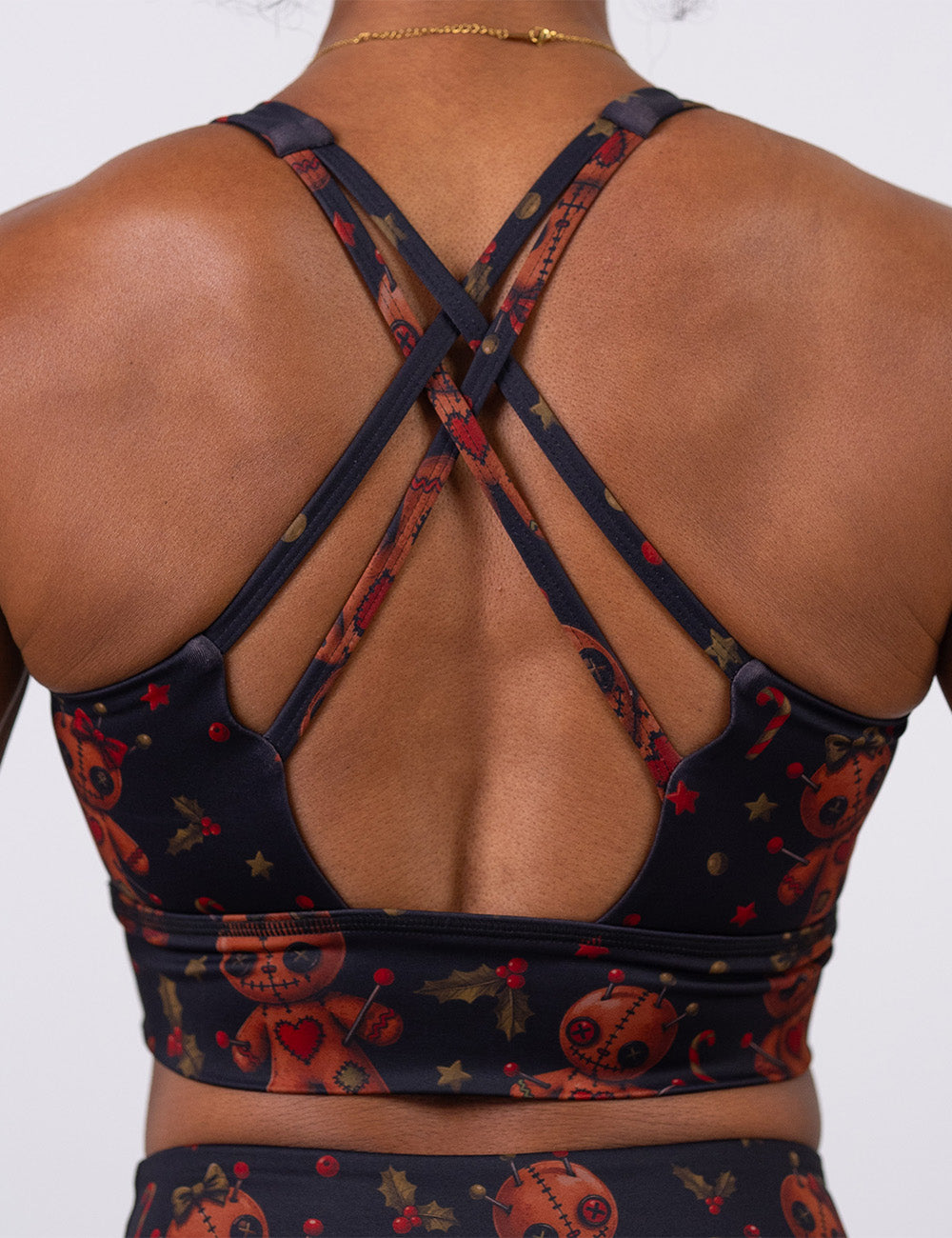 back of the gingerbread voodoo dolls with pins in them surrounded by berries and stars on a black background sports bra