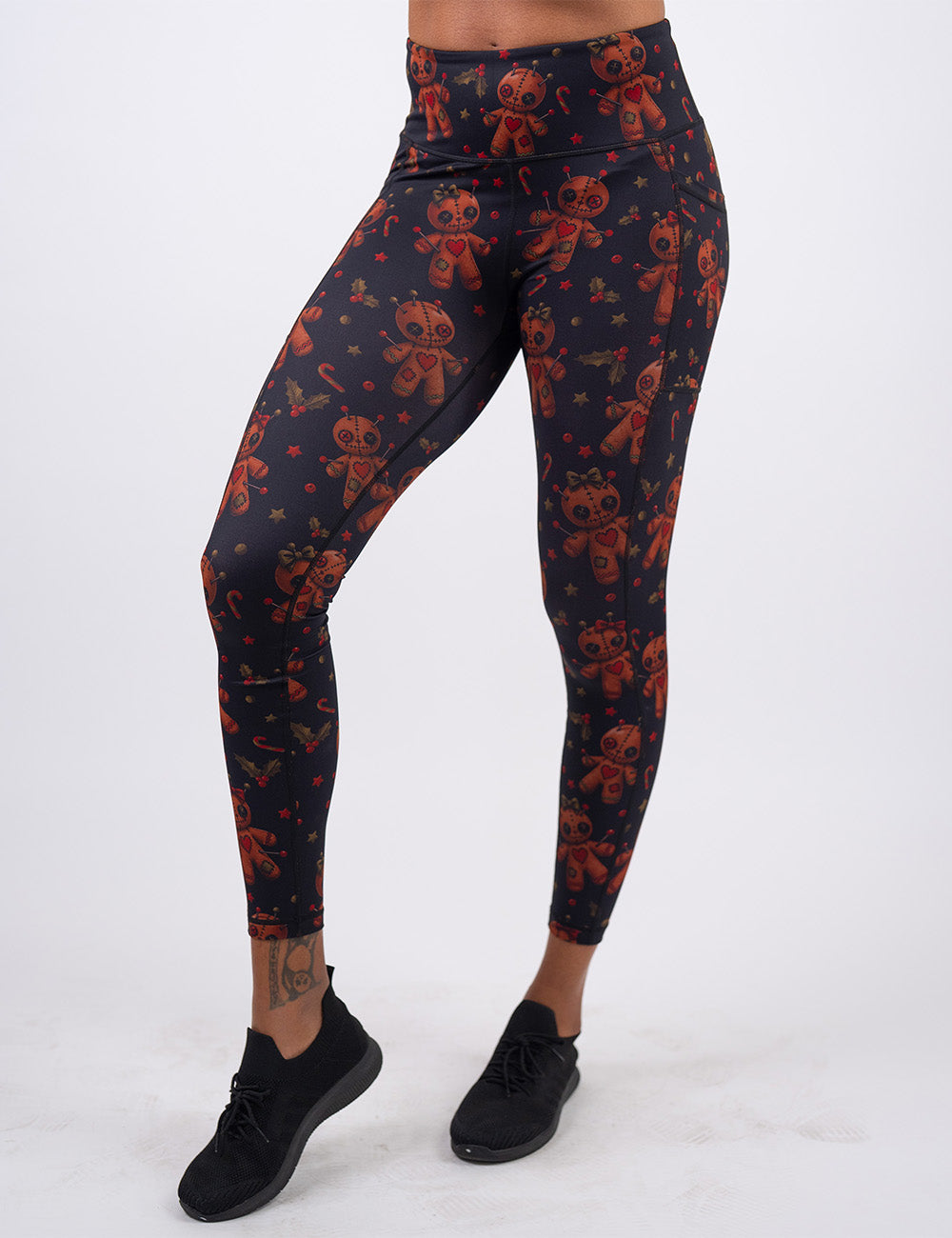 front of the gingerbread voodoo dolls with pins in them surrounded by berries and stars on a black background full length leggings