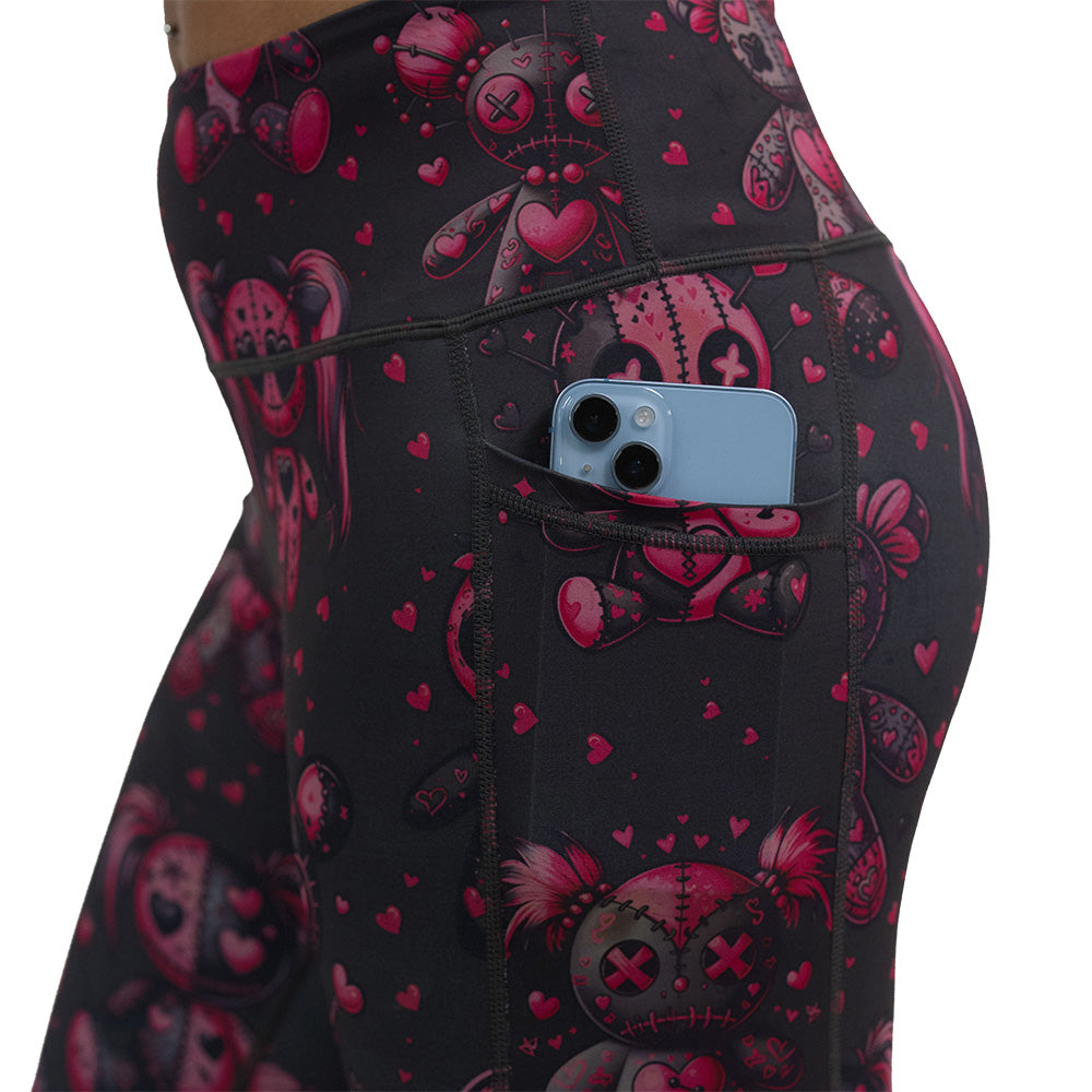 close up of the pocket of the pink voodoo doll with pink hearts pattern leggings with a phone in the pocket against a white background