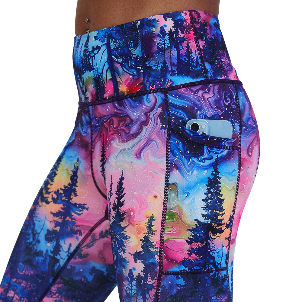 close up of the watercolor rainbow patterned forest leggings with a phone in the pocket against a white background