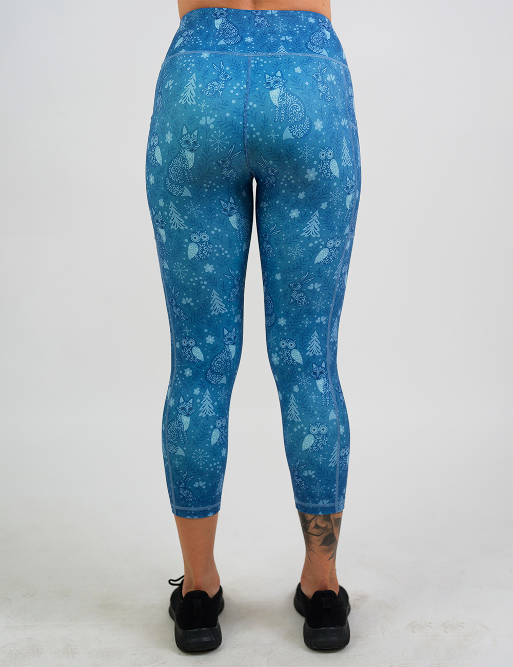 back of the blue foxes, owls, and bunnies in a winter landscape capri leggings against a white background