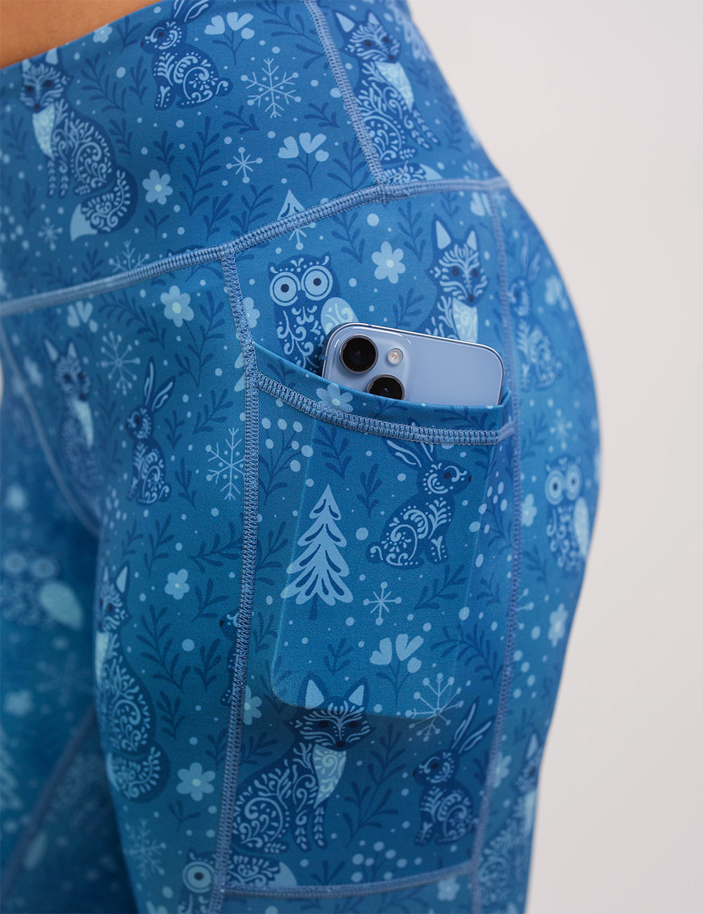 close up of the blue foxes, owls, and bunnies in a winter landscape leggings with a phone in its pocket