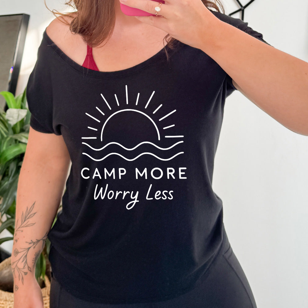 black slouchy tee with the words "camp more worry less" on it, under the line art graphic of a large sun over water
