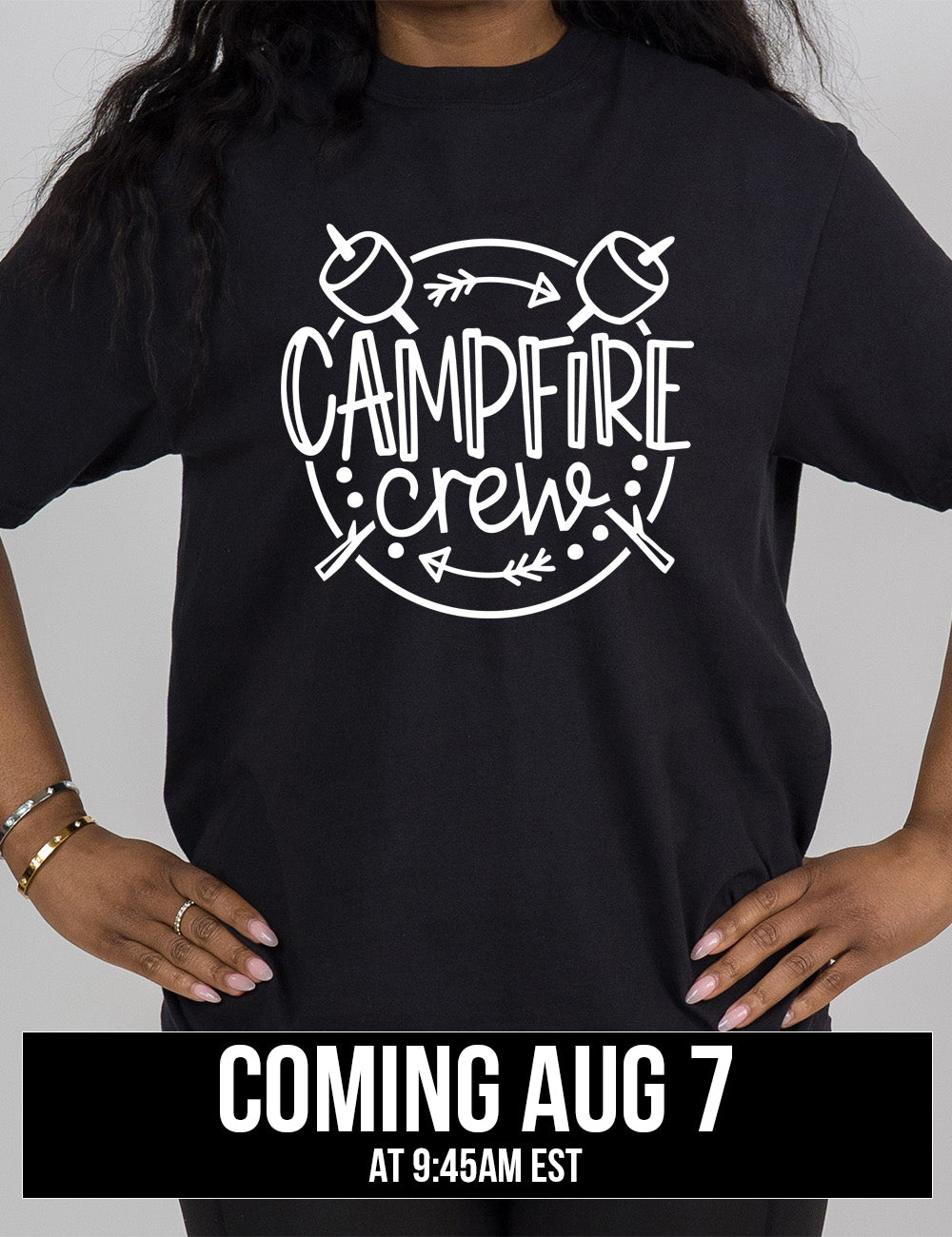 black modern tee with the words "campfire crew" in the middle of a circle, with a couple arrows and dots, and two marshmallows on sticks crossing behind the words coming august 7th
