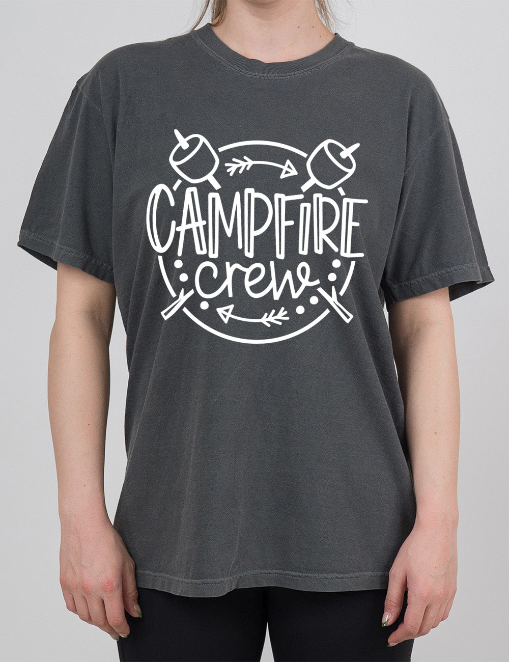 pepper modern tee with the words "campfire crew" in the middle of a circle, with a couple arrows and dots, and two marshmallows on sticks crossing behind the words
