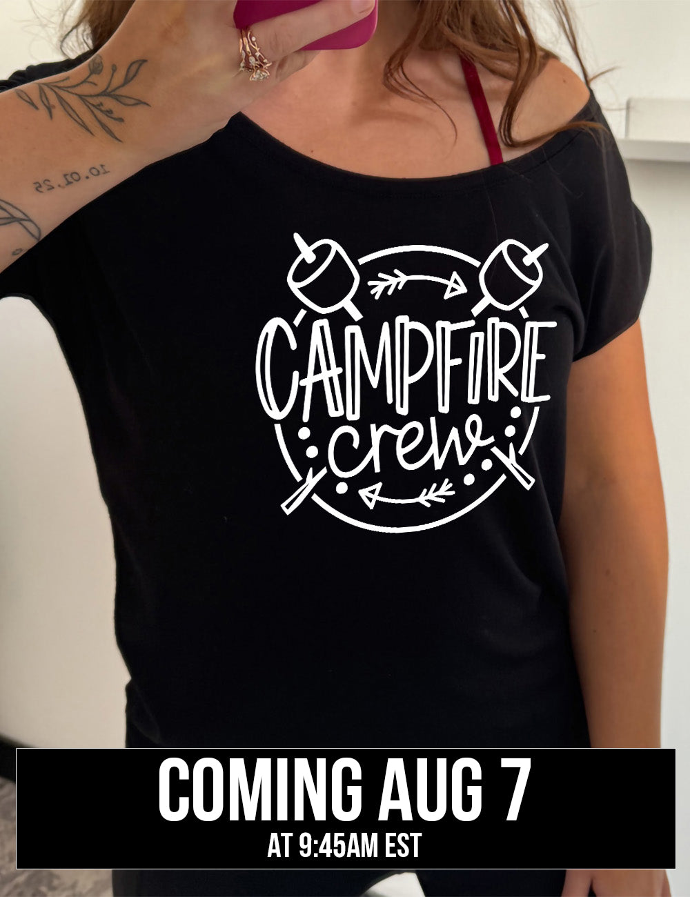 black slouchy tee with the words "campfire crew" in the middle of a circle, with a couple arrows and dots, and two marshmallows on sticks crossing behind the words coming august 7th