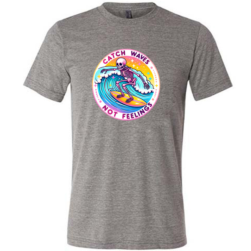 Grey colored shirt with a skeleton surfing graphic on it that says "Catch Waves Not Feelings" 