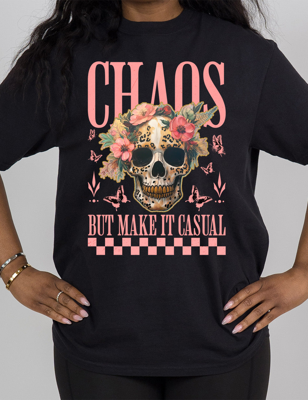 black modern tee with the print placement on the front, with the large word "chaos" on it, with the smaller words "but make it casual," and the graphic in between this of a gold-toothed skull with some leopard print, with a crown of flowers, surrounded by butterflies