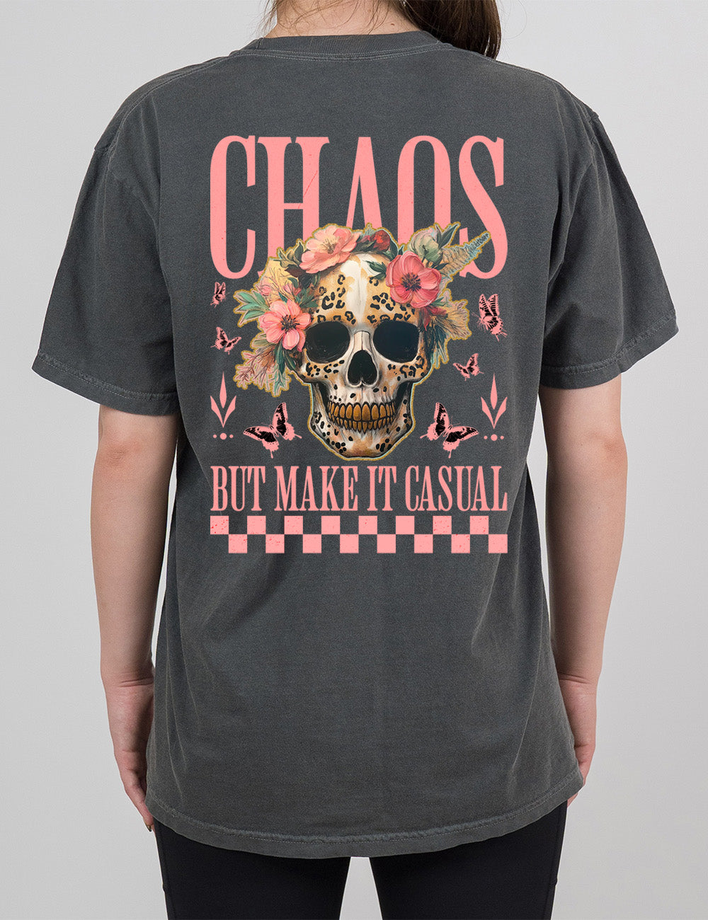 pepper modern tee with the print placement on the back, with the large word "chaos" on it, with the smaller words "but make it casual," and the graphic in between this of a gold-toothed skull with some leopard print, with a crown of flowers, surrounded by butterflies