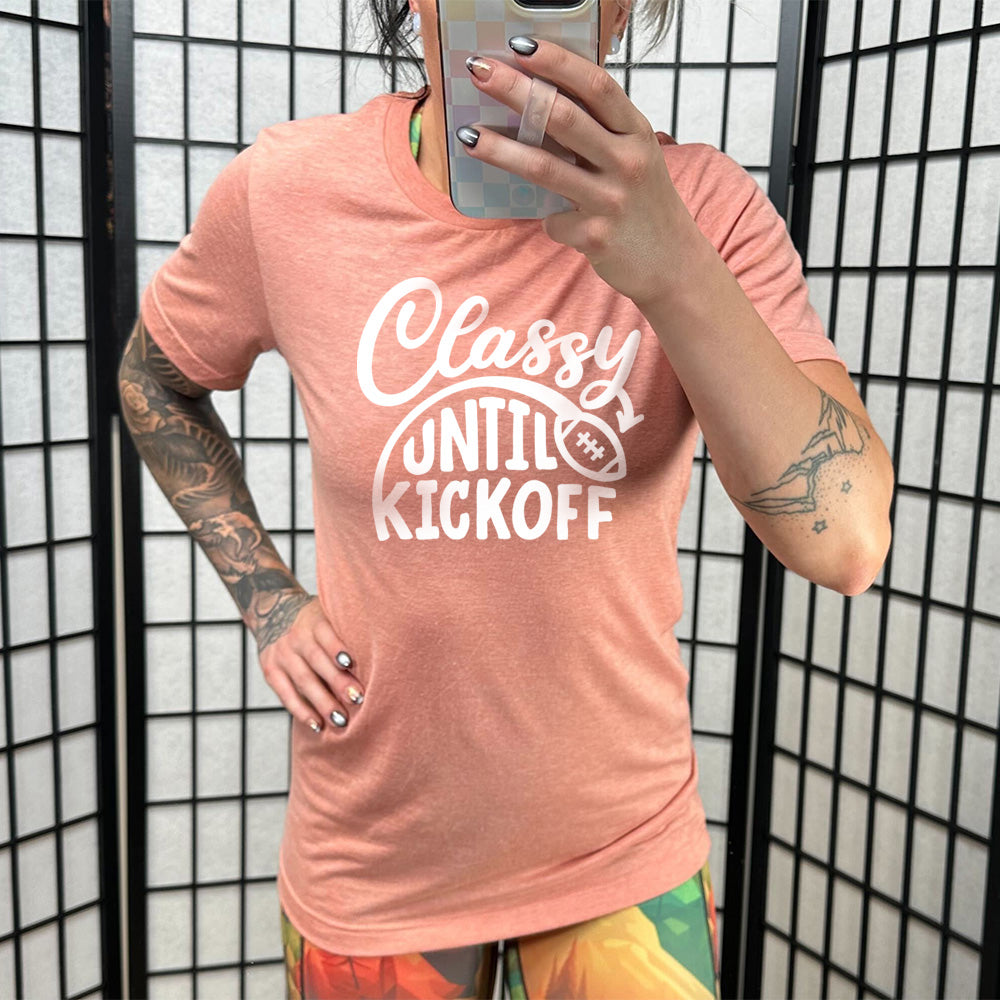 Model wearing sunset colored shirt with football graphic on it that says "Classy Until Kickoff"
