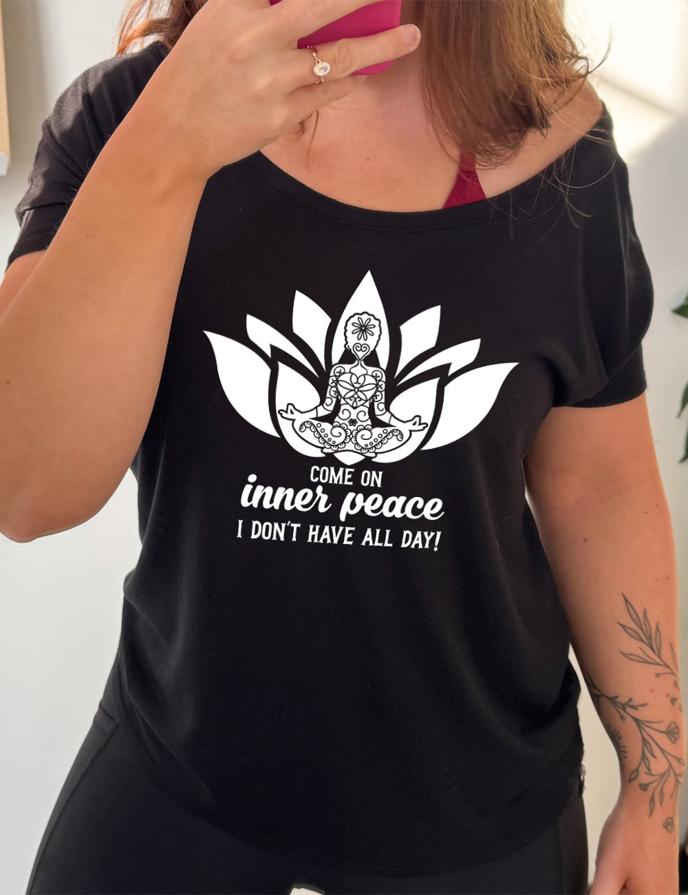 black slouchy tee with the graphic of a patterned person's silhouette doing a seated yoga pose, sitting in a lotus shape, with the words underneath saying "come on inner peace I don't have all day!"