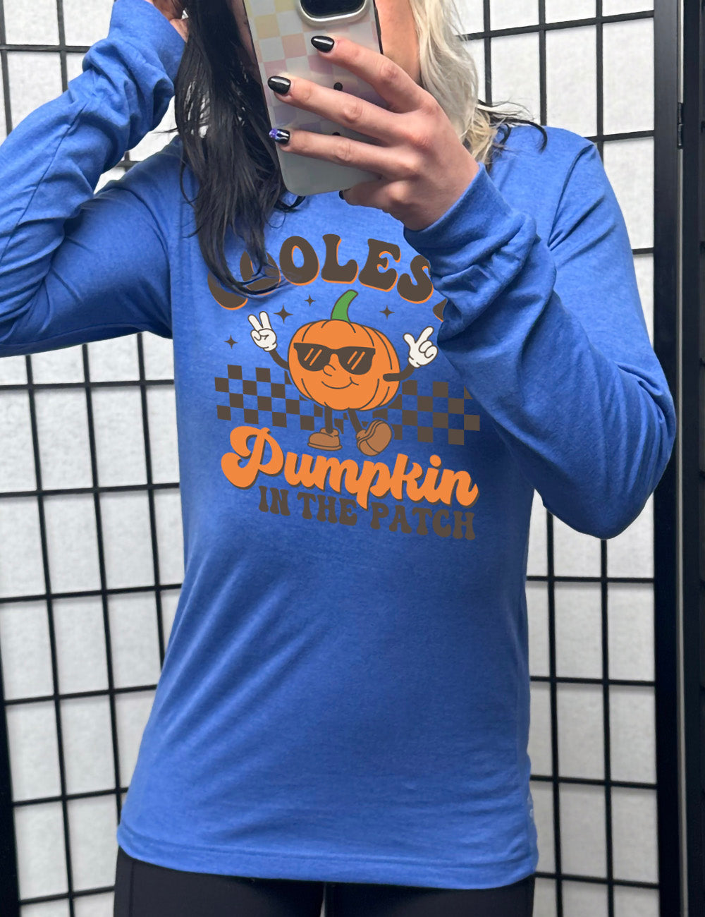 heather true royal long sleeve with the graphic of a pumpkin, wearing sunglasses, both arms raised, foot kicking out, in front of a checkered banner, surrounded by a few little stars, with the words around it saying "coolest pumpkin in the patch"