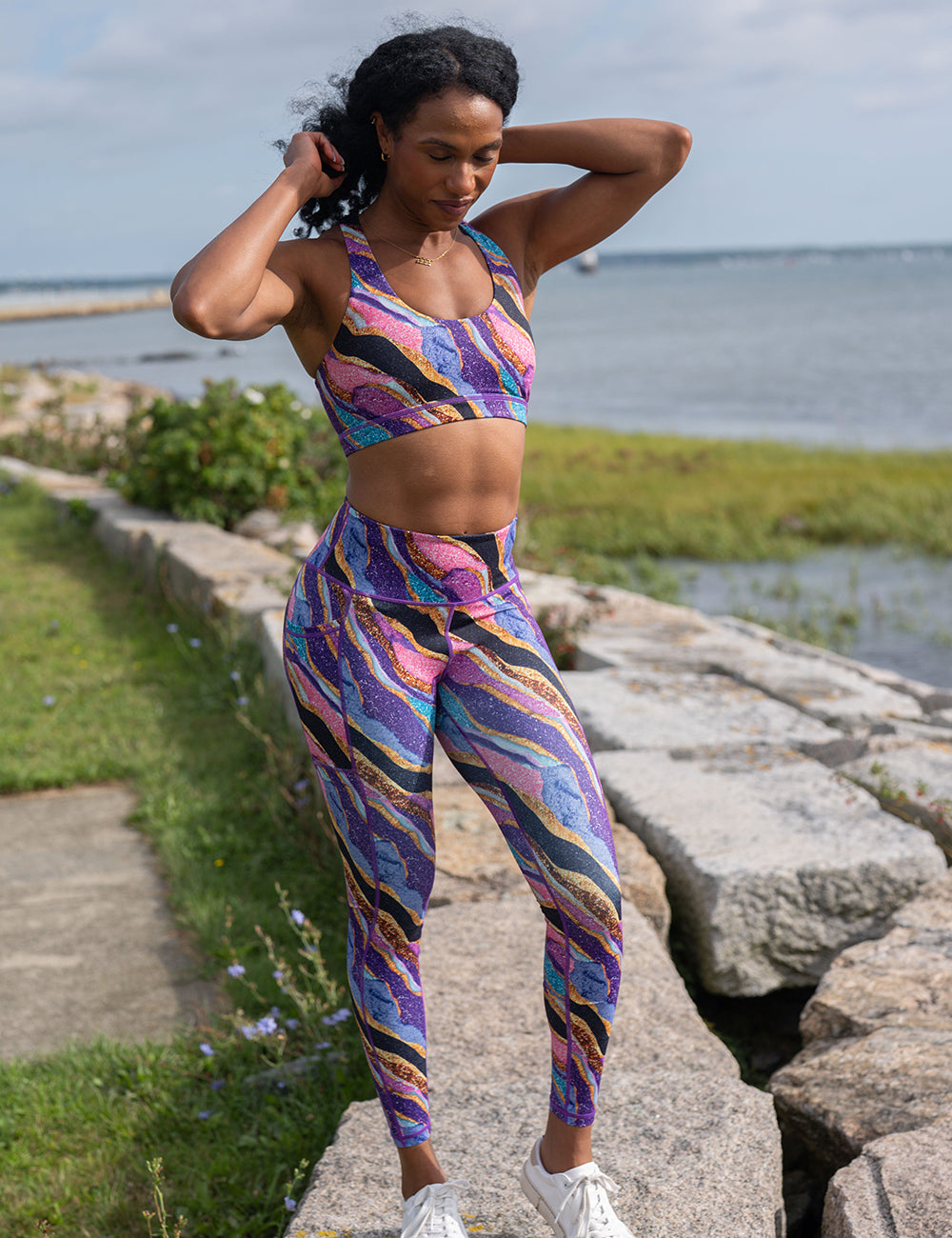 model wearing the purple, gold, black, blue, and pink abstract stripes sports bra and full length leggings