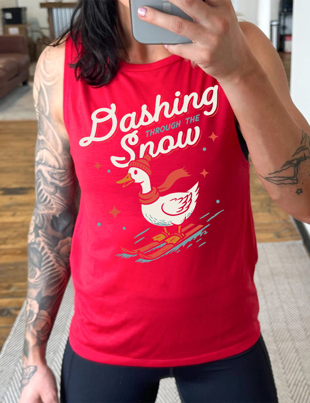 red muscle tank with the graphic of a goose, wearing a hat and scarf, on skis, in  downwards motion,  with some stars, and the words above it saying "Dashing through the Snow" 