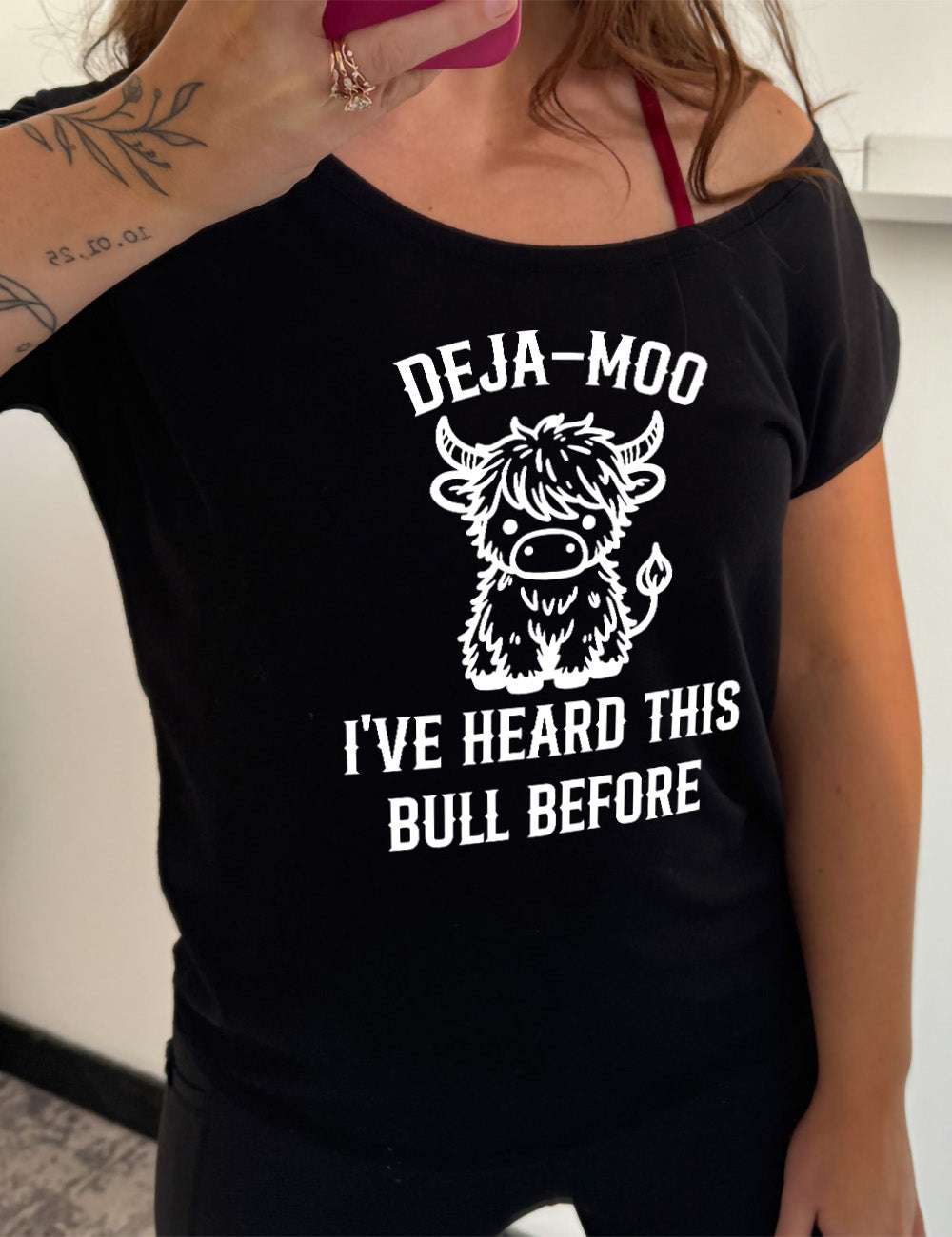 black slouchy tee with the words "deja-moo I've heard this bull before" on it, around the graphic of a bull, sitting facing forward