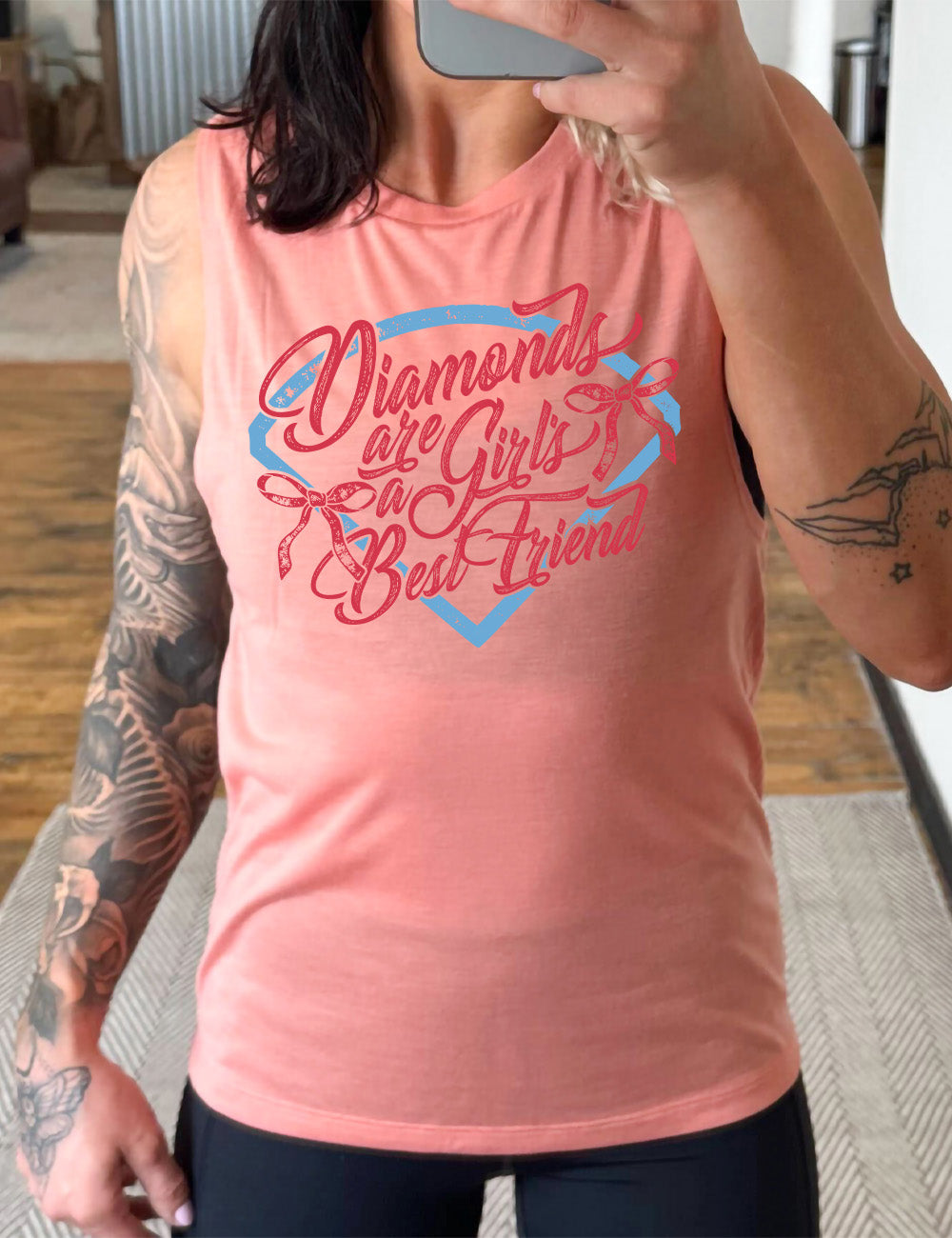 peach muscle tank with the words "diamonds are a girl's best friend" on it, with two bows, all in front of a baseball diamond