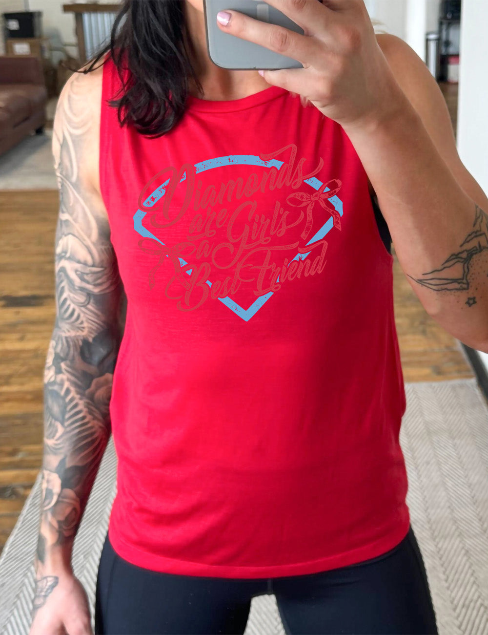 red muscle tank with the words "diamonds are a girl's best friend" on it, with two bows, all in front of a baseball diamond