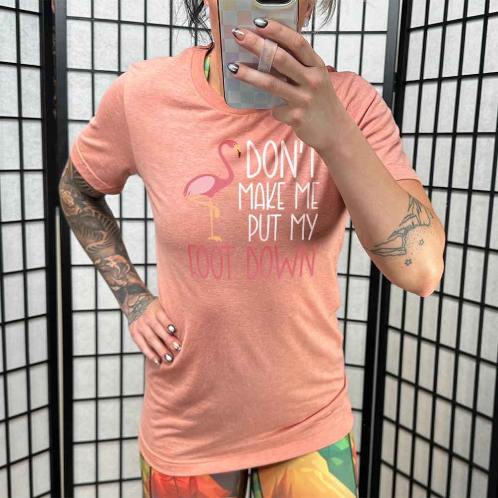 sunset unisex tee with the words "don't make me put my foot down" on it, with the graphic of a flamingo next to the words, with its foot raised