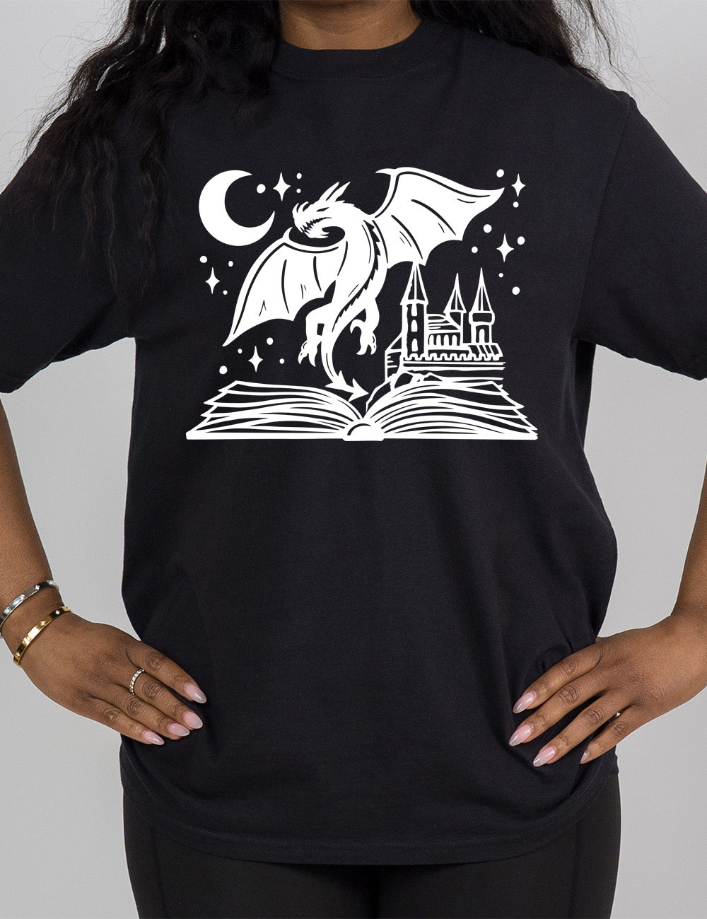 black modern tee with the graphic of dragon flying out of an open book into a night sky of stars and crescent moon, with a castle also rising out of the book