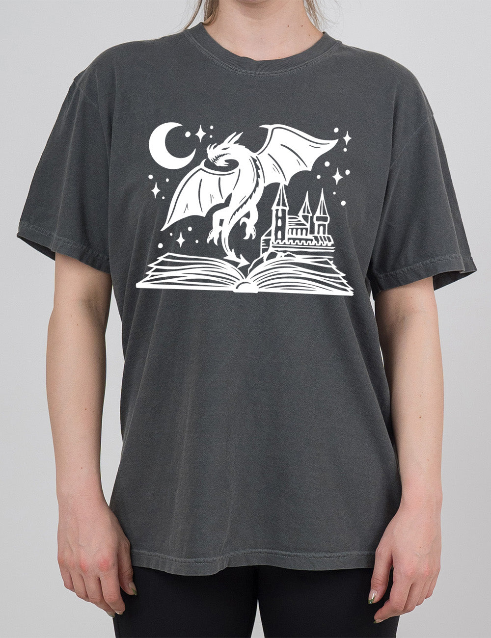 grey modern tee with the graphic of dragon flying out of an open book into a night sky of stars and crescent moon, with a castle also rising out of the book