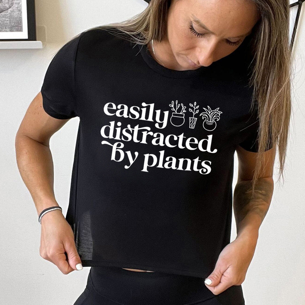 Model wearing black colored cropped top with a potted plant graphic on it that says "Easily Distracted By Plants"
