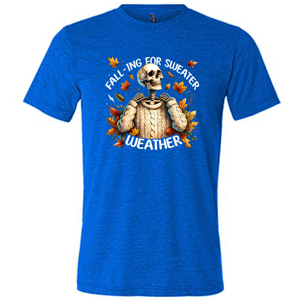 Blue colored shirt with fall leaves and skeleton wearing a sweater graphic on it that says "Fall-ing For Sweater Weather"