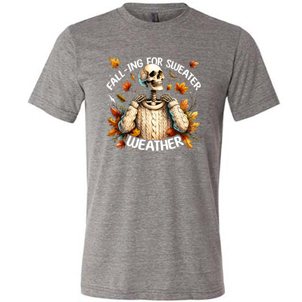 Grey colored shirt with fall leaves and skeleton wearing a sweater graphic on it that says "Fall-ing For Sweater Weather"