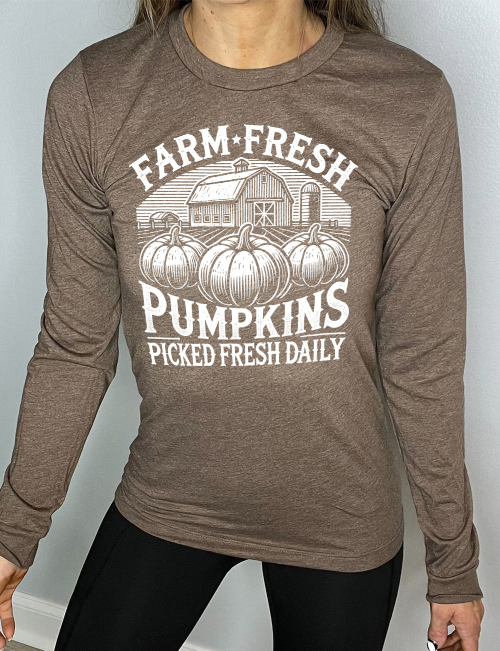 heather brown long sleeve shirt with the words "farm fresh pumpkins picked fresh daily" around the graphic of a barn in the background and three pumpkins in the foreground