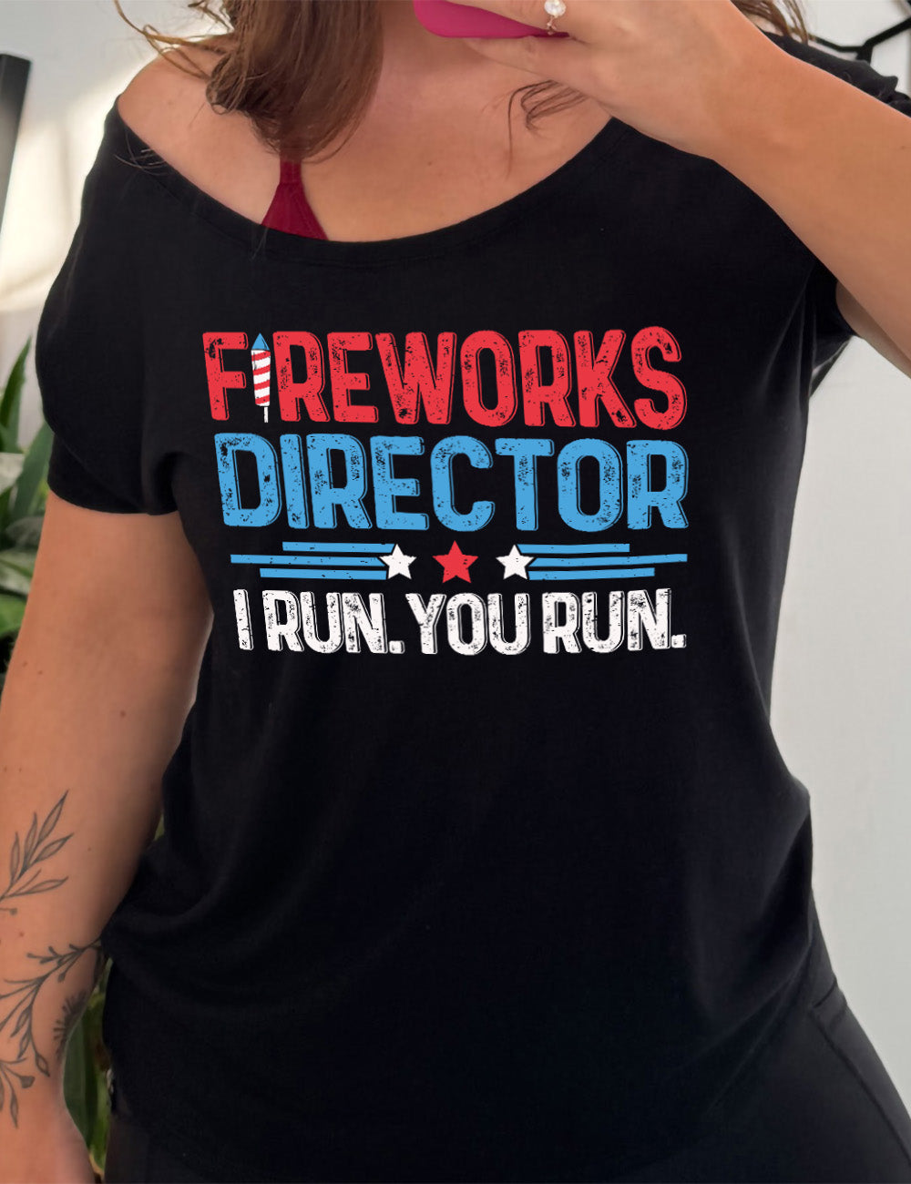 black slouchy tee with the words "Fireworks Director -- I run. You run." on it, with the "i" of "fireworks" in the shape of a firework, and some stripes with a few stars in between the word "director" and "I run. You run."