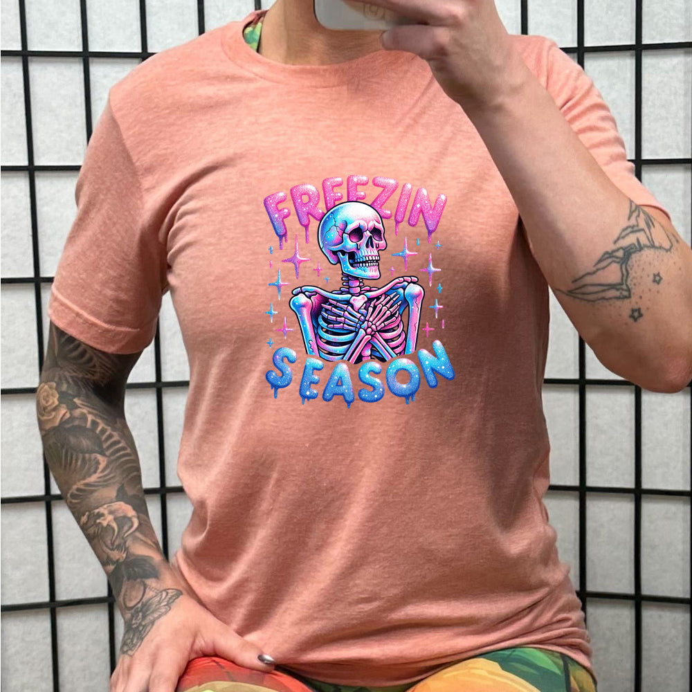 peach shirt with the text "freezin season" with a graphic of a skeleton on it