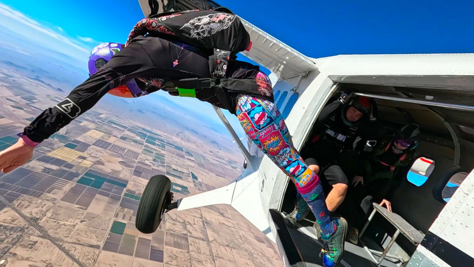 Person skydiving from an airplane with a clear blue sky and landscape below.