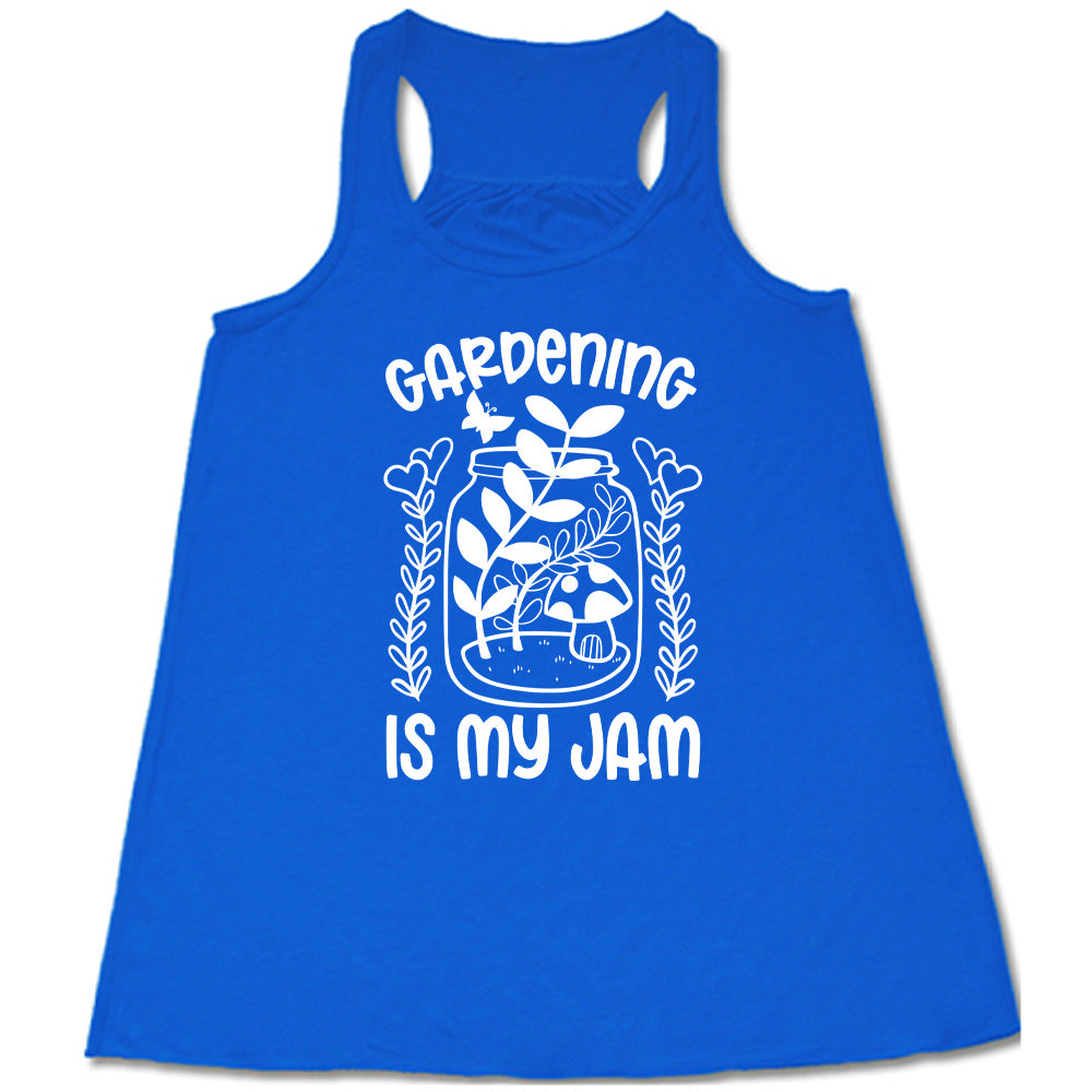 blue flowy racerback tank with the words "gardening is my jam" on it, and the graphic of a jar with plants and a mushroom in it, a little butterfly flying above it, and a plant (with hearts for flowers on them) on both sides of it