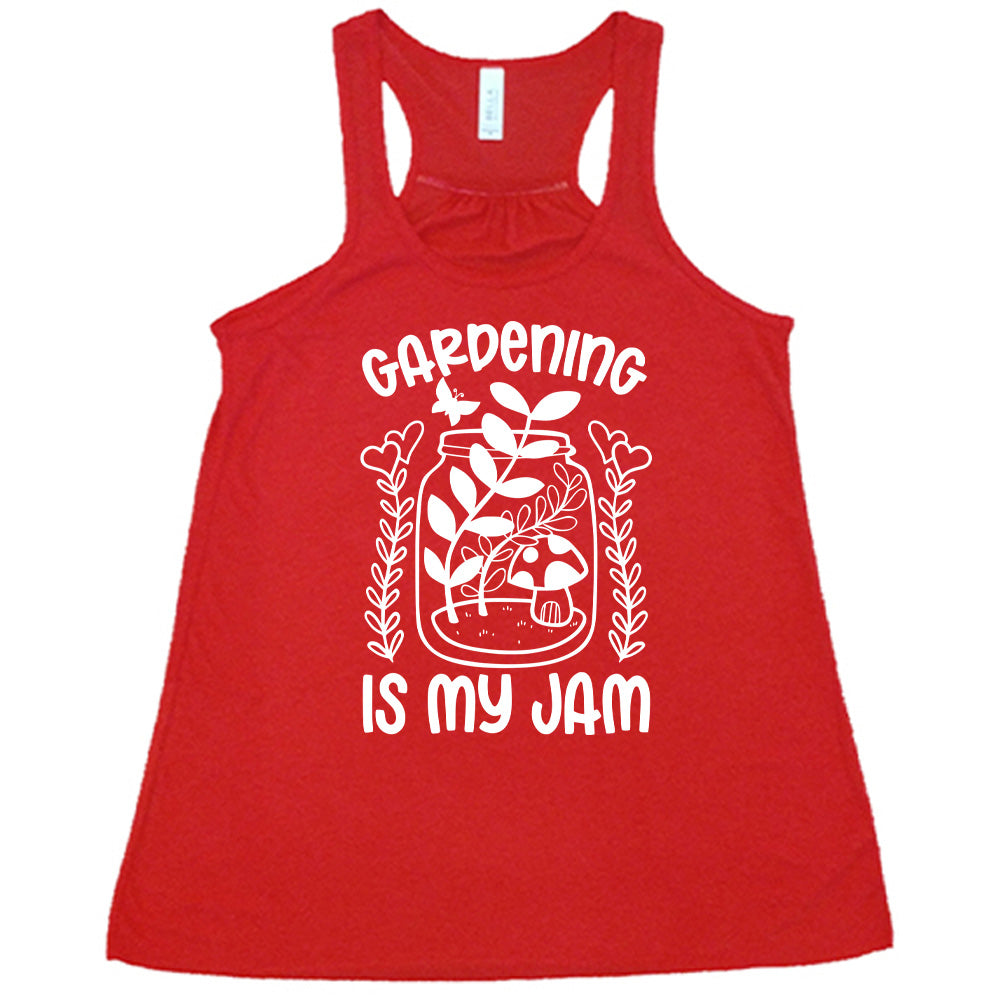 red flowy racerback tank with the words "gardening is my jam" on it, and the graphic of a jar with plants and a mushroom in it, a little butterfly flying above it, and a plant (with hearts for flowers on them) on both sides of it