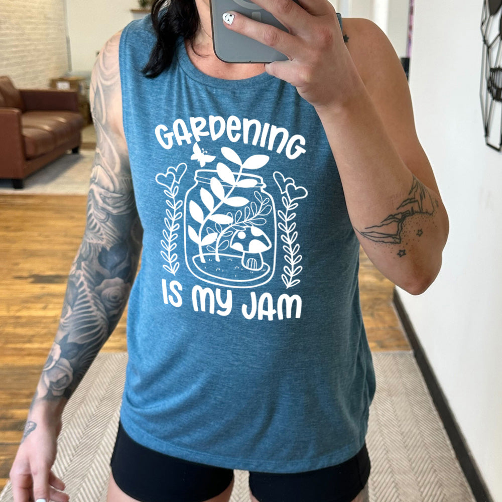 deep teal muscle tank with the words "gardening is my jam" on it, and the graphic of a jar with plants and a mushroom in it, a little butterfly flying above it, and a plant (with hearts for flowers on them) on both sides of it