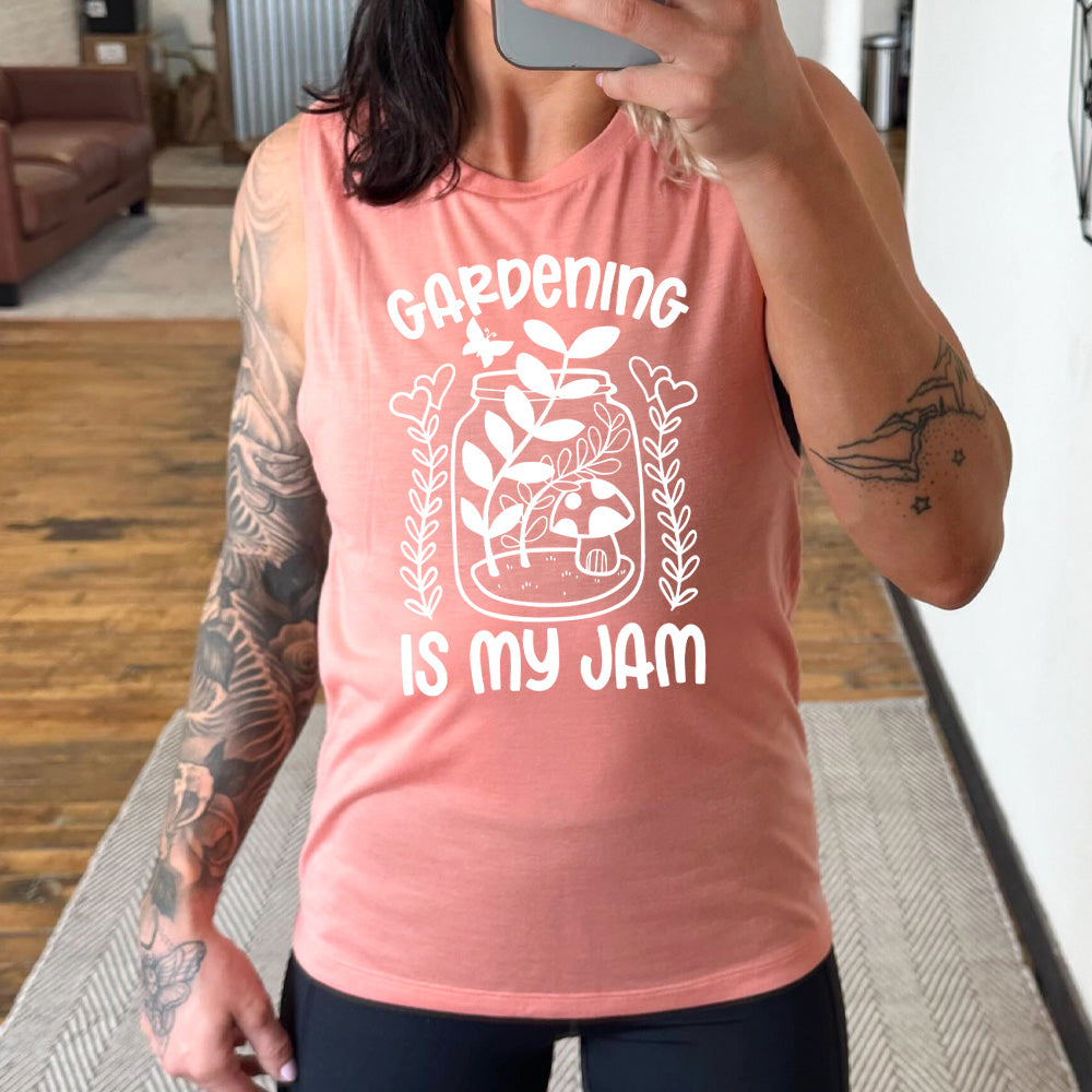peach muscle tank with the words "gardening is my jam" on it, and the graphic of a jar with plants and a mushroom in it, a little butterfly flying above it, and a plant (with hearts for flowers on them) on both sides of it
