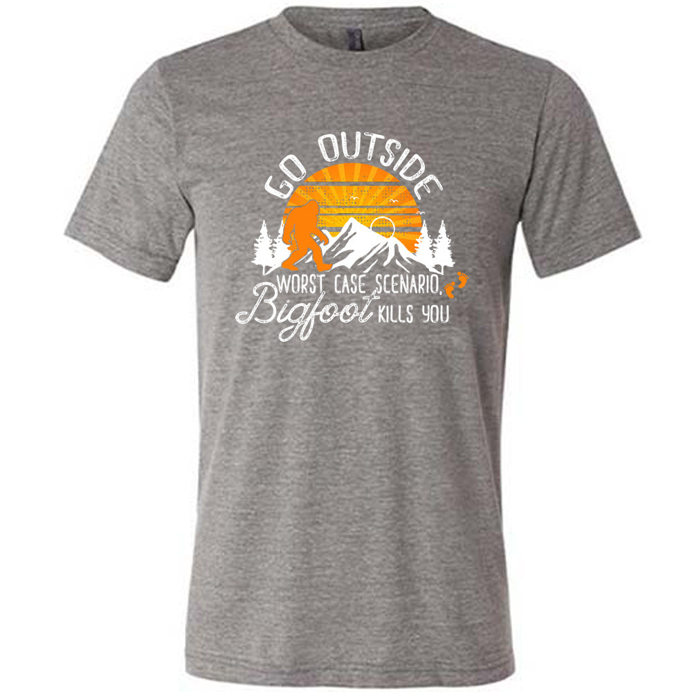 Grey colored shirt with sun and bigfoot in mountains graphic on it that says "Go Outside, Worst Case Scenario Bigfoot Kills You"