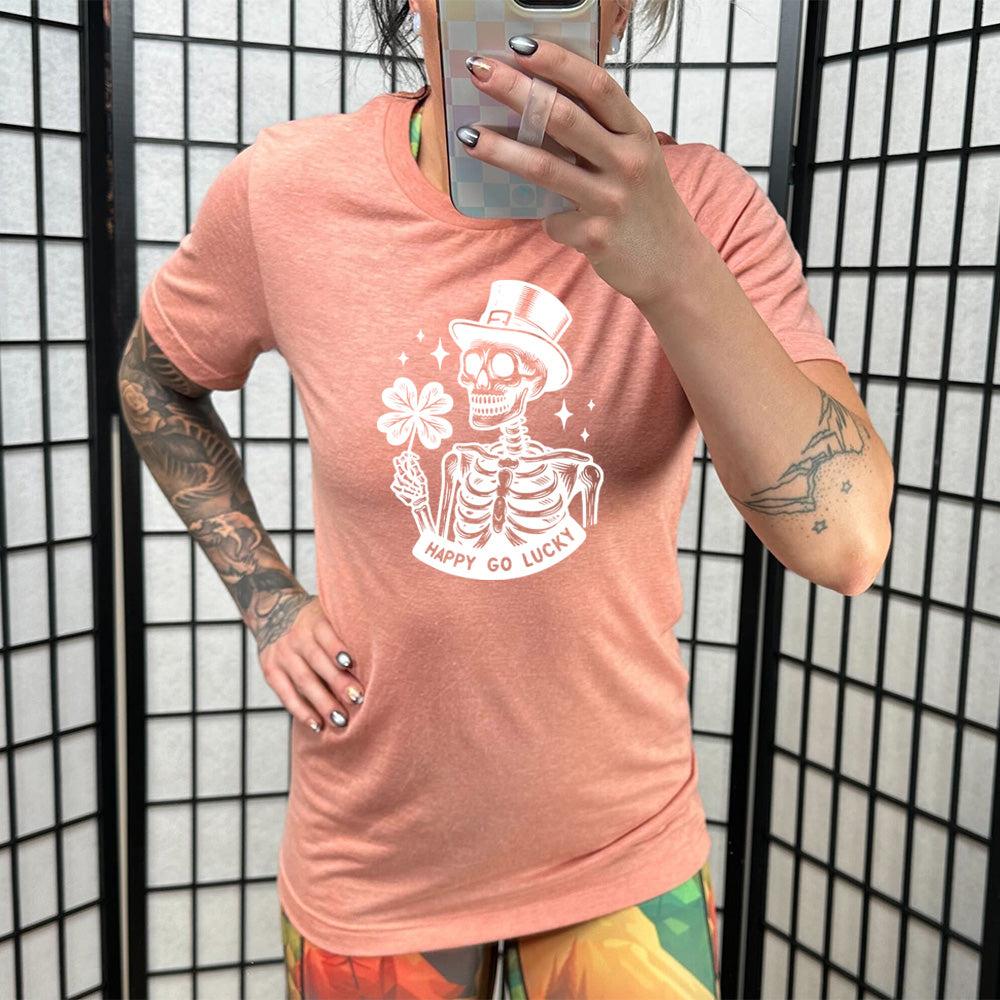 coral shirt with a skeleton graphic and the text "happy go lucky" on it