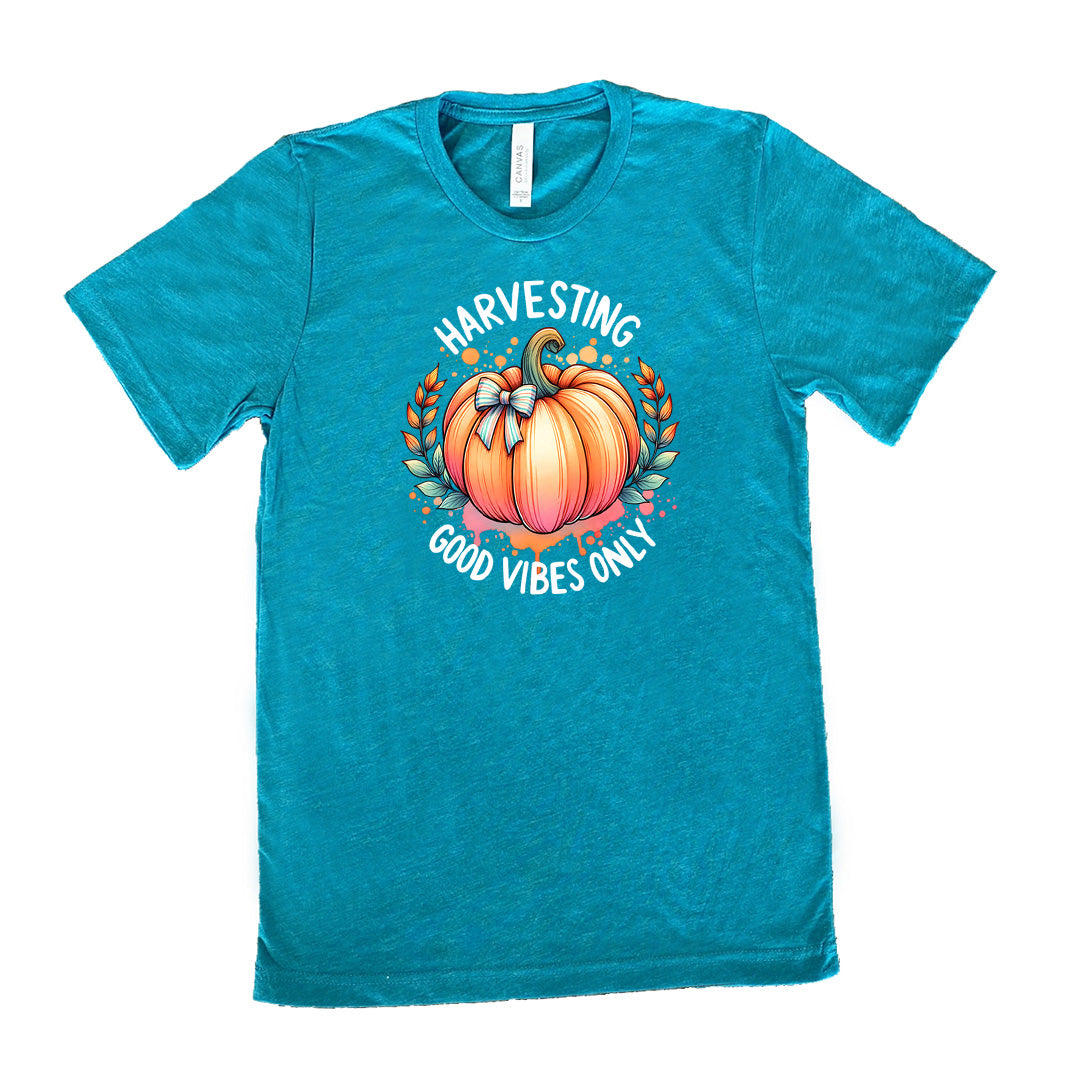 Teal colored shirt with pumpkin graphic on it that says "Harvesting Good Vibes Only"