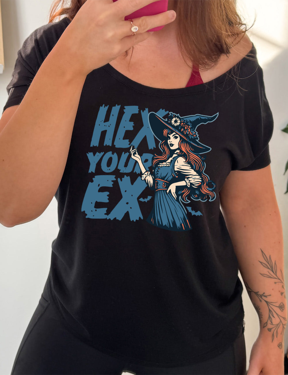 black slouchy tee with the words "hex your ex" on it, next to the detailed, colorful graphic of a long-haired witch, hand on hip, other hand raised, wearing a flowery witch hat, and an old-fashioned dress