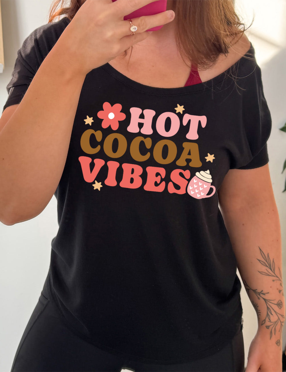 black slouchy tee with the colorful words saying "HOT COCOA VIBES" with small graphics of a flower and mug, with many hearts on it, topped with whipped cream, and a few stars