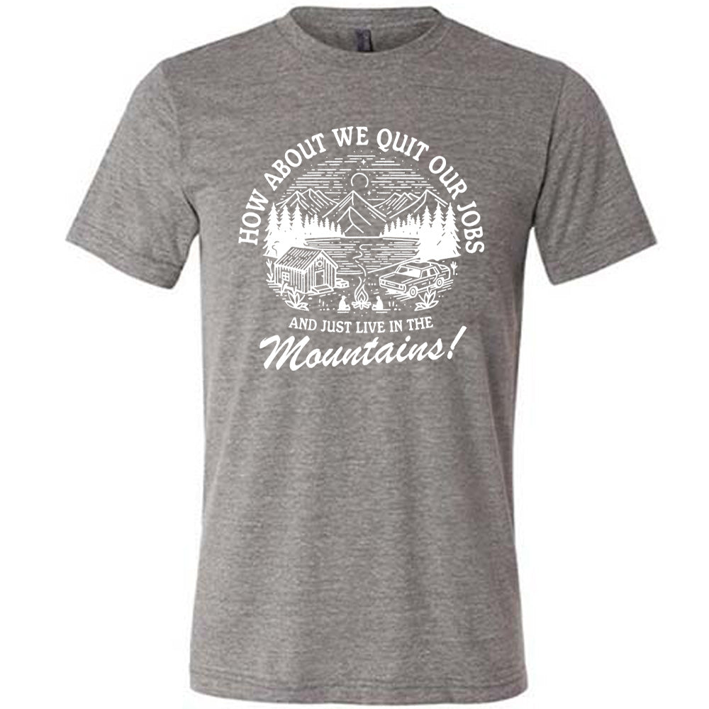 grey unisex tee with the words "How about we quit our jobs and just live in the mountains!" on it, with the graphic of a small house, a couple people sitting around a campfire, and an old car in the woods and mountains, with a sky and a couple stars and the moon