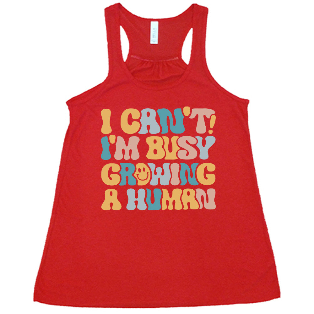 red racerback flowy tank with the words "I can't! I'm busy growing a human" on it in colorful font, with a smiley face in the "o" of the word "growing"