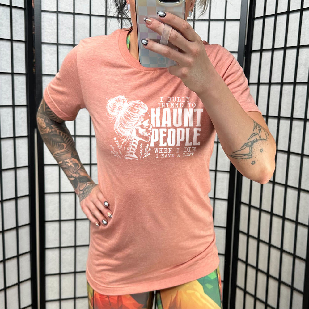 Model wearing sunset colored shirt with smiling female skeleton graphic on it that says "I Fully Intend To Haunt People When I Die I Have A List"