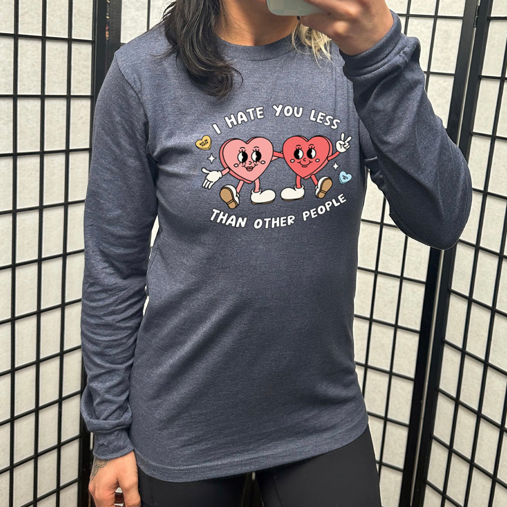 heather navy long sleeve shirt with the text "I Hate You Less Than Other People" on it, and the graphics of two heart people, arms on each other, smiling