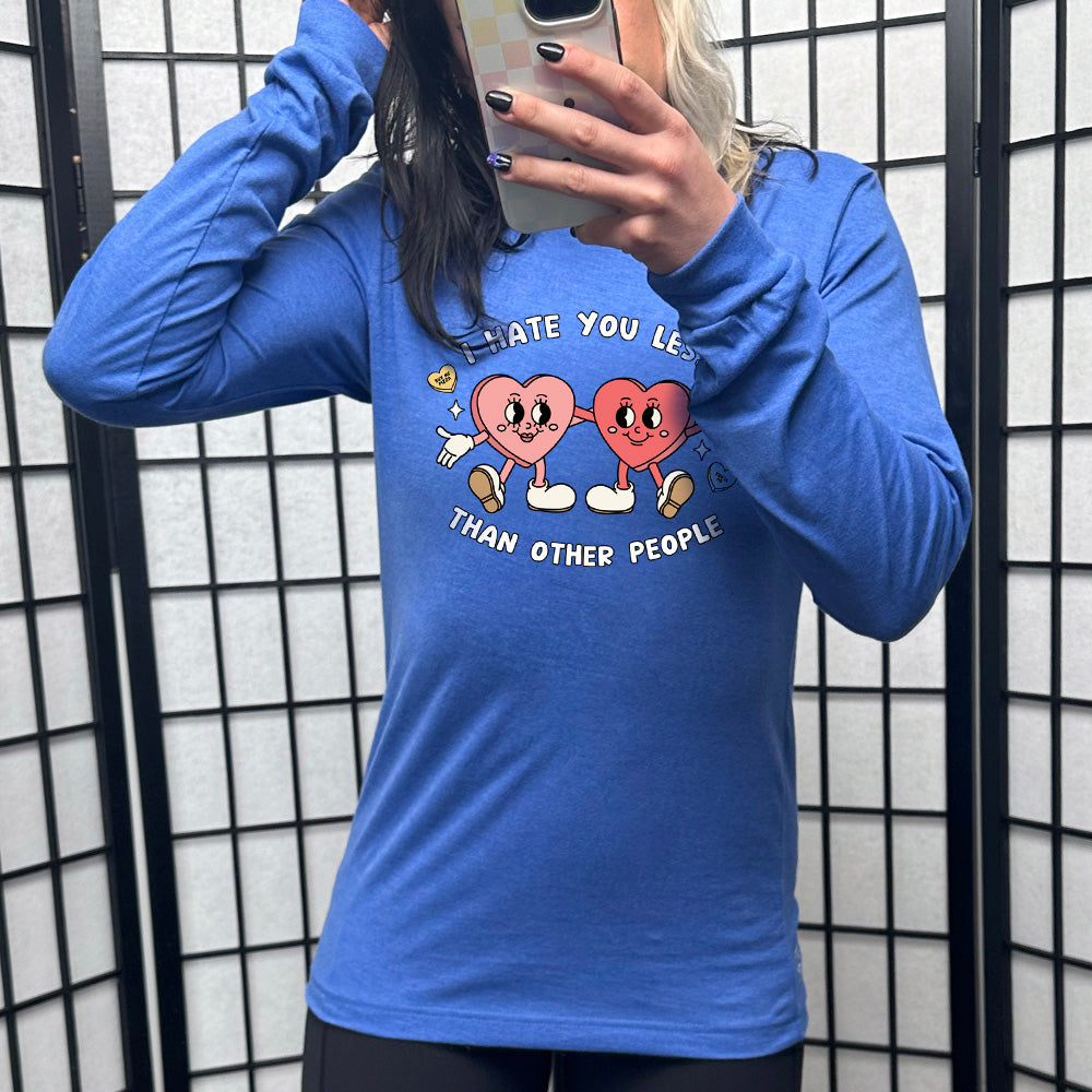 heather true royal long sleeve shirt with the text "I Hate You Less Than Other People" on it, and the graphics of two heart people, arms on each other, smiling