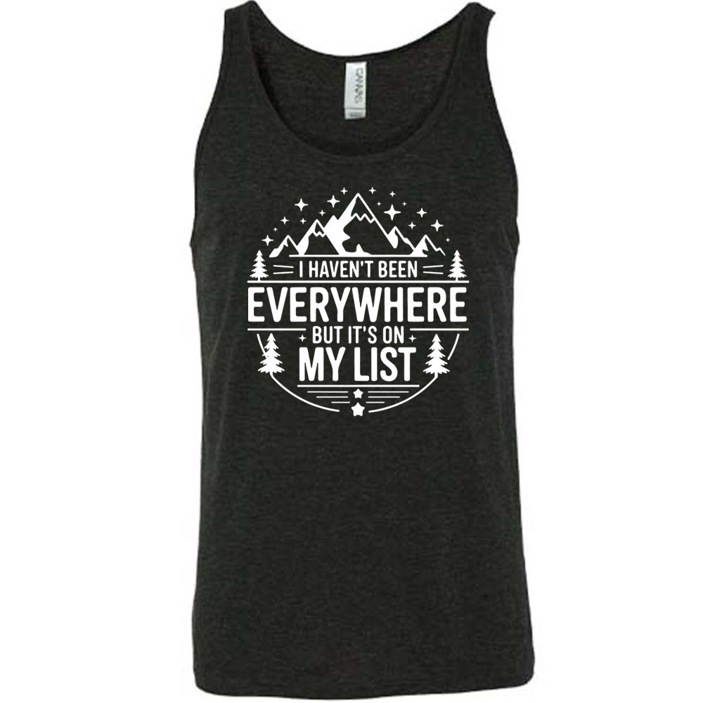 black unisex tank with the words "I haven't been everywhere but it's on my list" as part of a circular design involving the graphic of small mountains on top and a few trees on the sides and stars scattered around