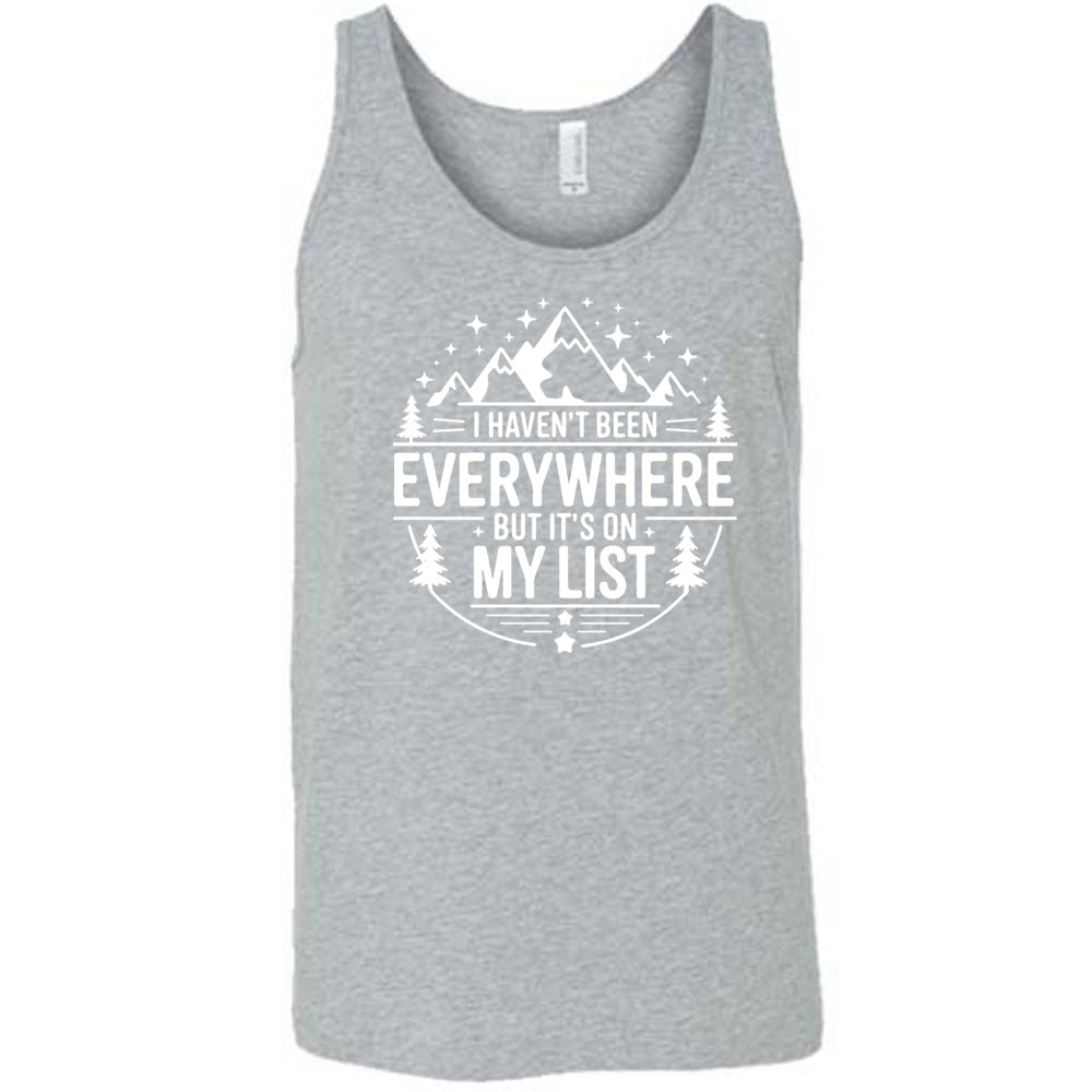 grey unisex tank with the words "I haven't been everywhere but it's on my list" as part of a circular design involving the graphic of small mountains on top and a few trees on the sides and stars scattered around