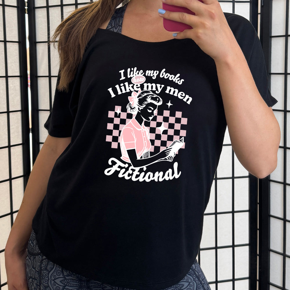 Black slouchy tee with the words "I like my books like I like my men Fictional" with the graphics of a woman in 1950s era attire reading a book in front of a checkered background